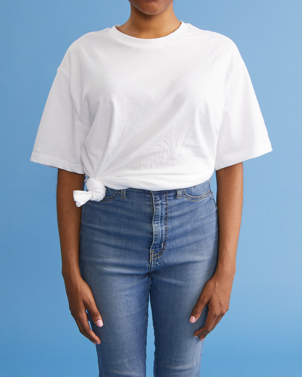 comment attacher un nœud latéral de chemise, femme avec les mains sur le côté portant une chemise blanche et un jean
