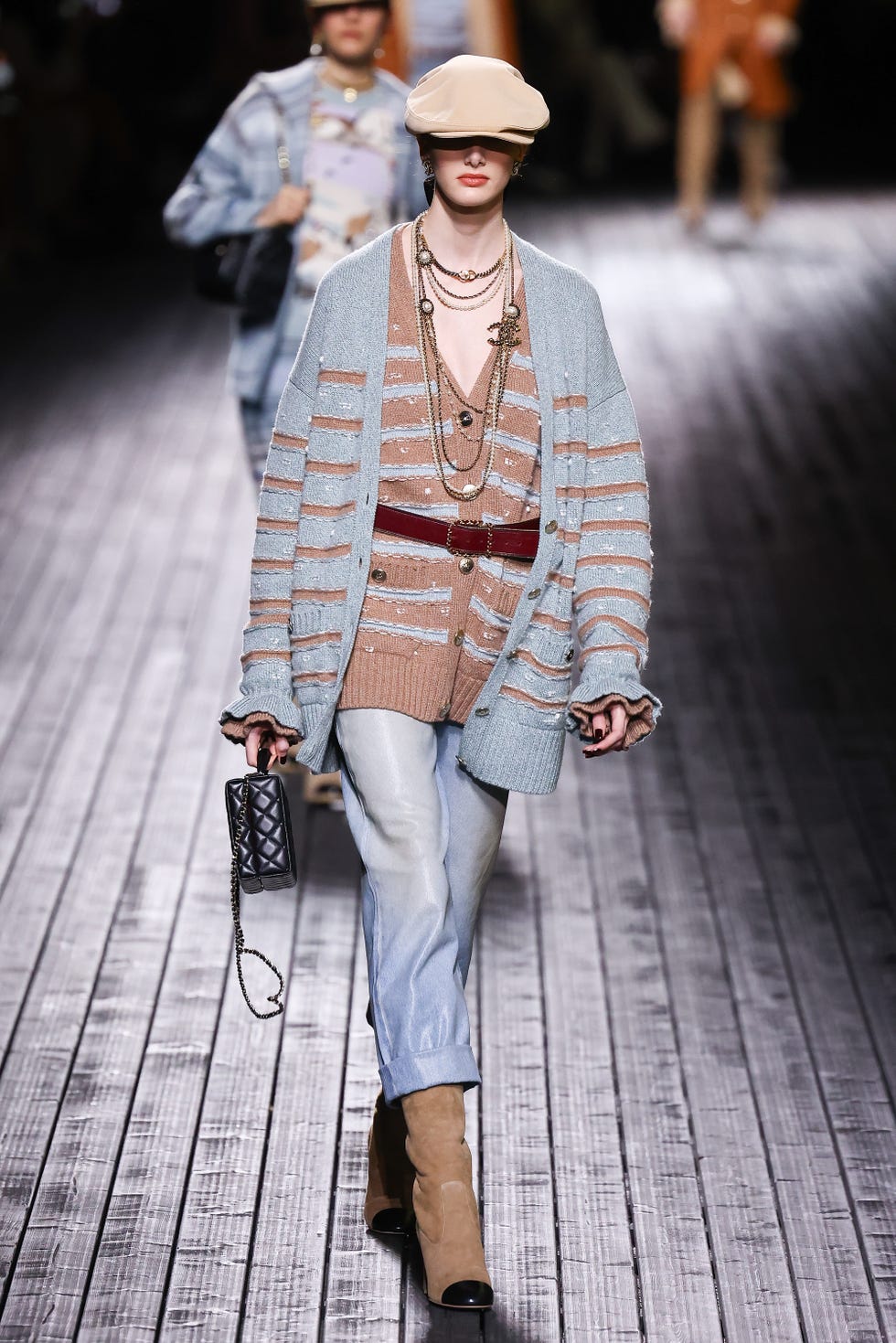 un mannequin portant deux cardigans rayés superposés ceinturés à la taille avec des bottes en jean en daim et une casquette sur le défilé chanel rtw automne 2024 dans un tour d'horizon des meilleures tenues de cardigan 2024