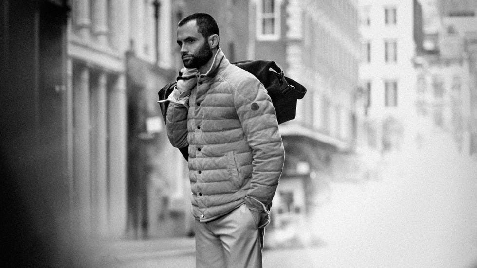 une personne portant une veste matelassée et tenant un sac se tient dans une rue