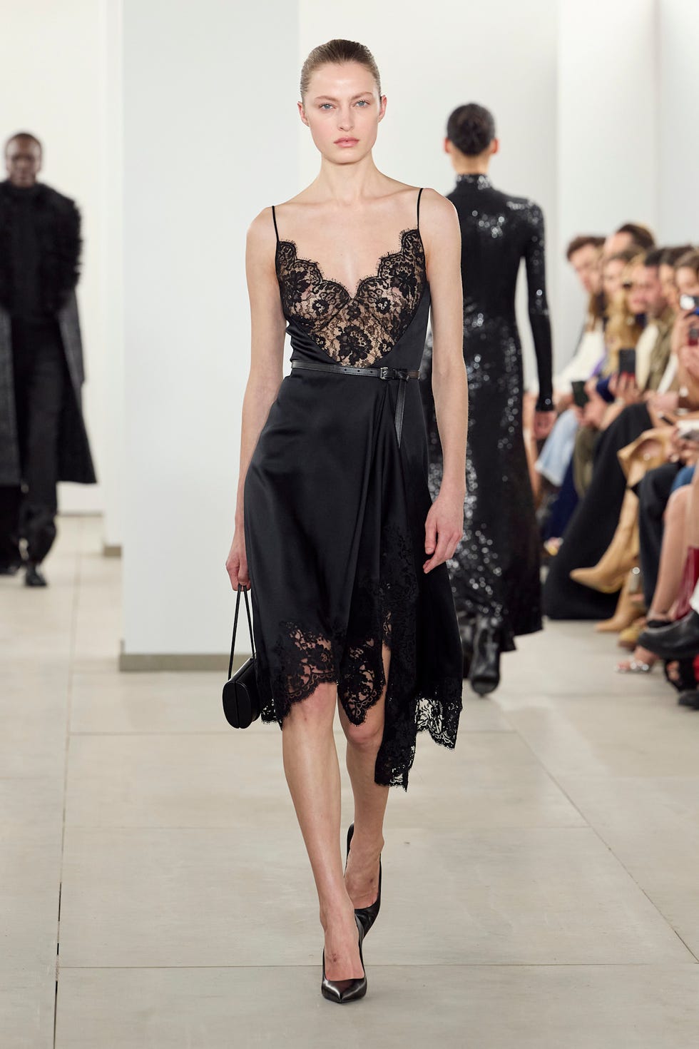 Modèle de défilé présentant une robe noire avec des détails en dentelle