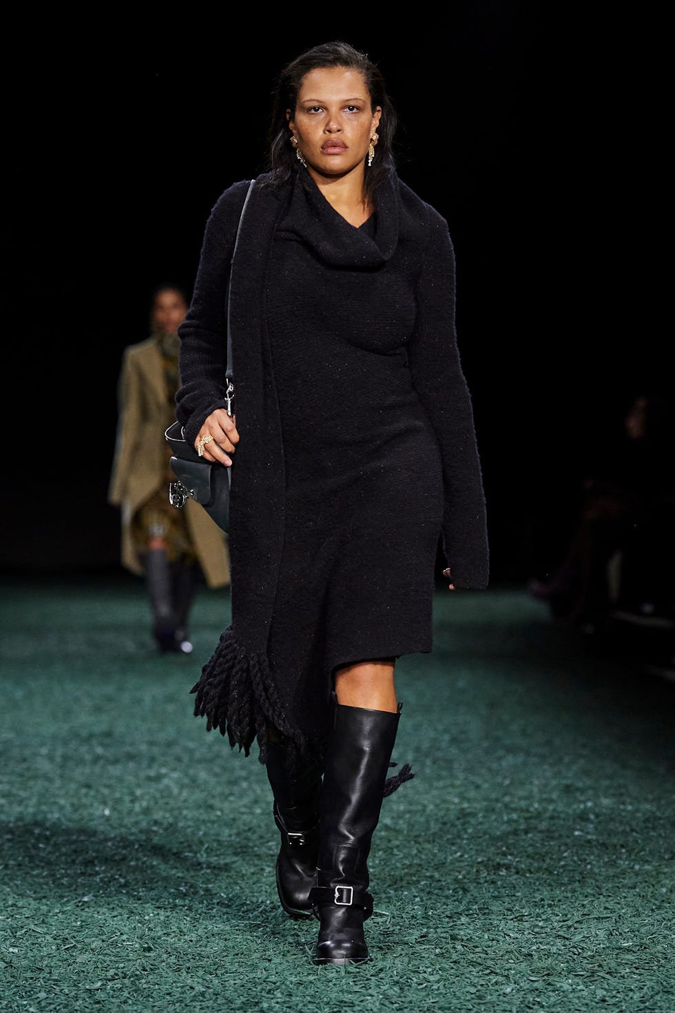 Modèle de mode marchant sur une piste portant une tenue noire et des bottes hautes