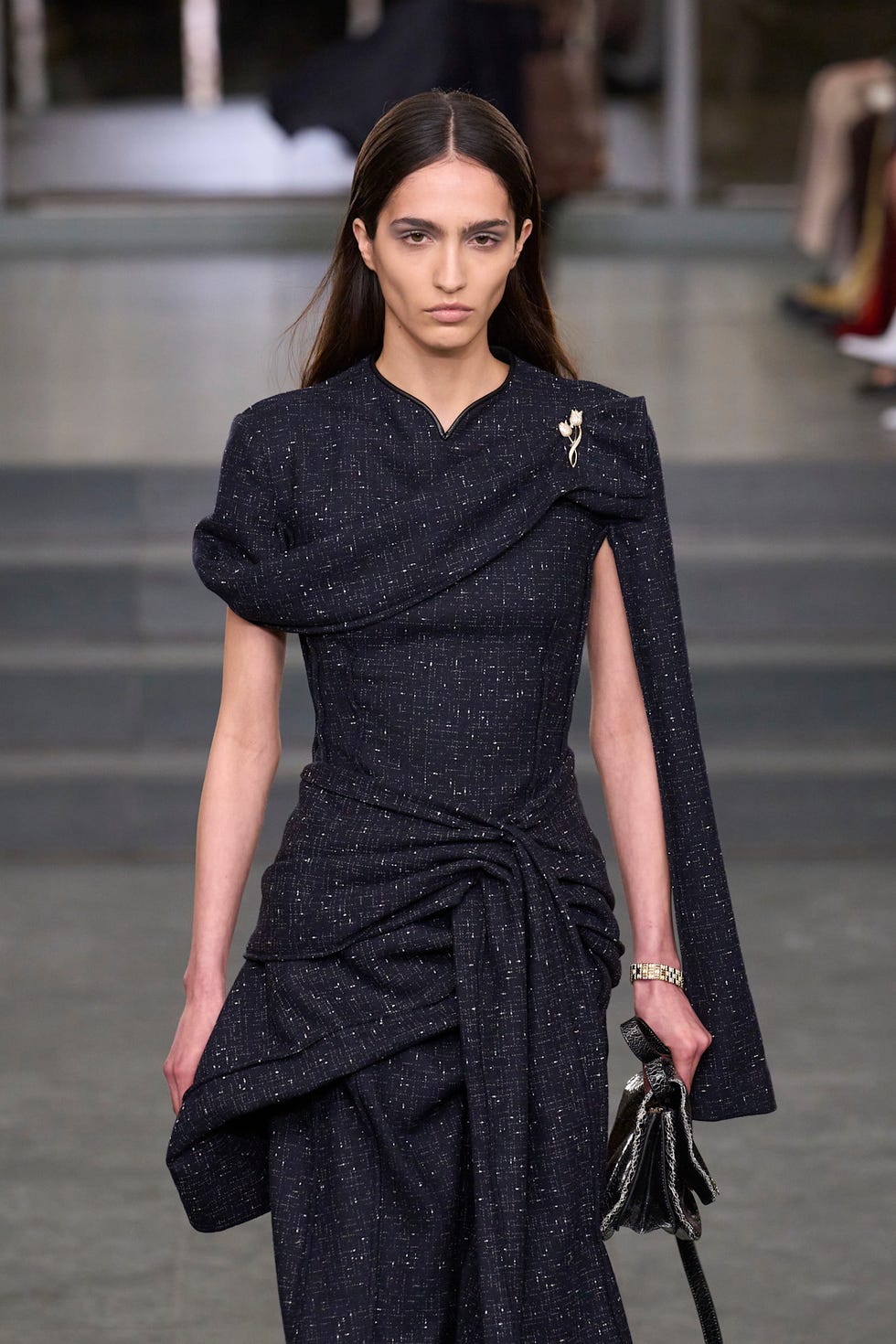 Femme vêtue d'une tenue sombre élégante avec un drapage de tissu complexe et une broche