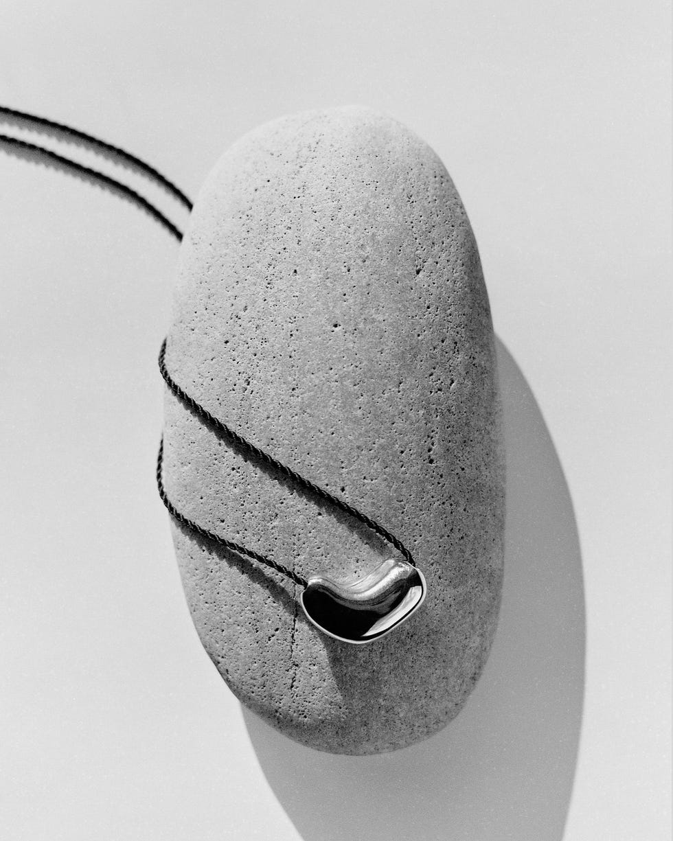 Une pierre ovale lisse avec un cordon noir et un pendentif métallique courbe brillant attaché