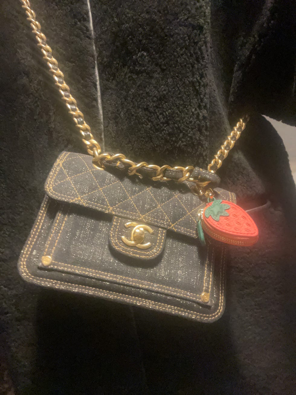 Sac à main Chanel avec une texture en jean et une sangle de chaîne en or avec un charme de fraise