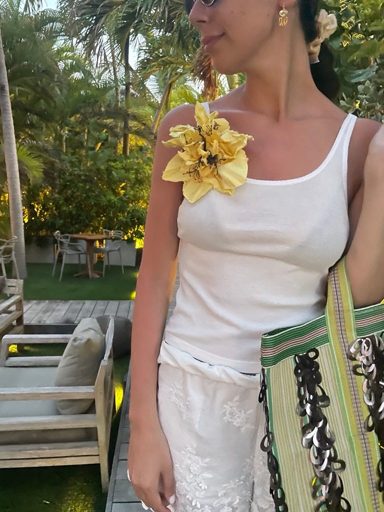 Une femme portant un haut blanc et un accessoire floral tenant un sac coloré