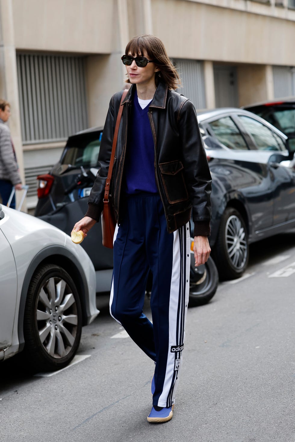 paris, france 29 septembre : un invité porte un pull bleu à col en V, une veste en cuir marron, un pantalon de survêtement adidas à rayures bleues, des baskets bleues, un sac en cuir marron, à l'extérieur de hodakova, pendant le printemps été 2026 de vêtements pour femmes dans le cadre de la fashion week de paris le 29 septembre 2025 à paris, france. (photo de Claudio lavenia/getty images)